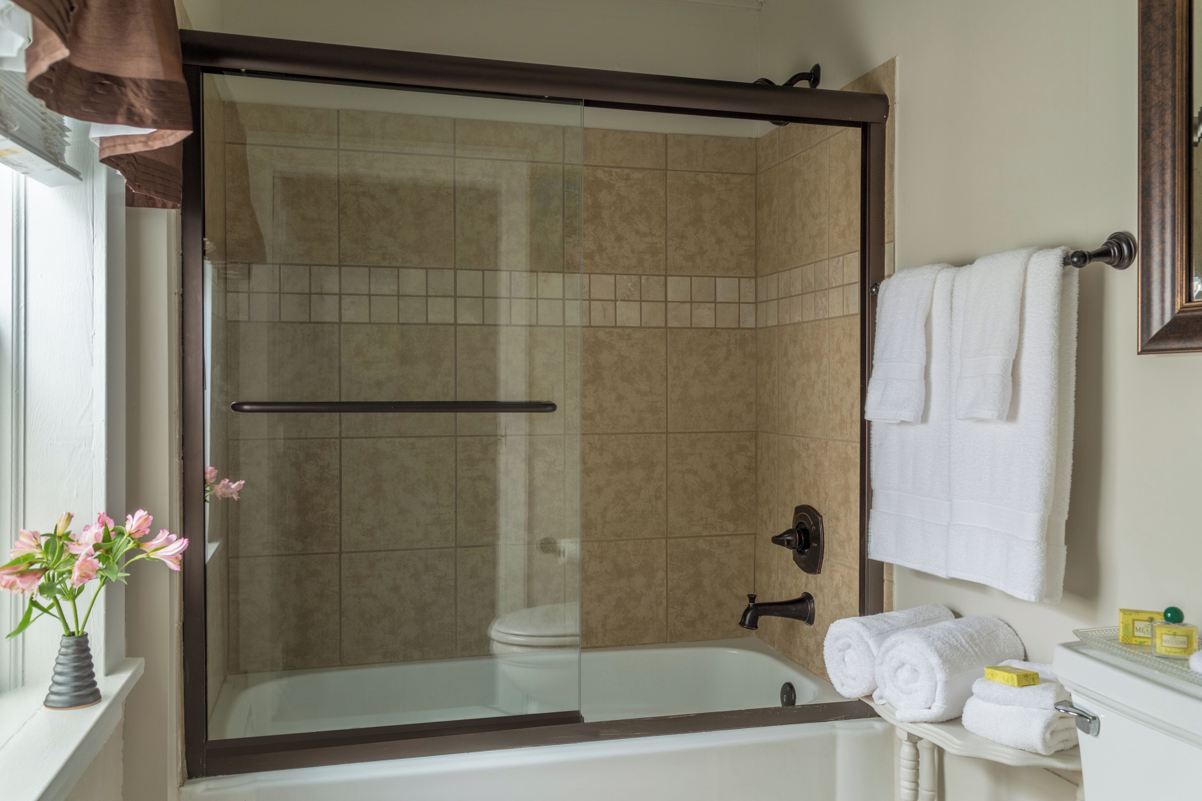 A bathroom with a glass-enclosed shower, a white bathtub, a towel rack, and a small shelf with toiletries.