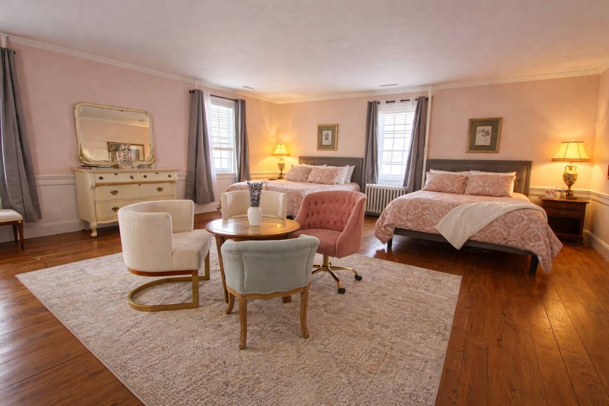 A bedroom with two beds, a dresser, a vanity, and a sitting area with chairs and a table.