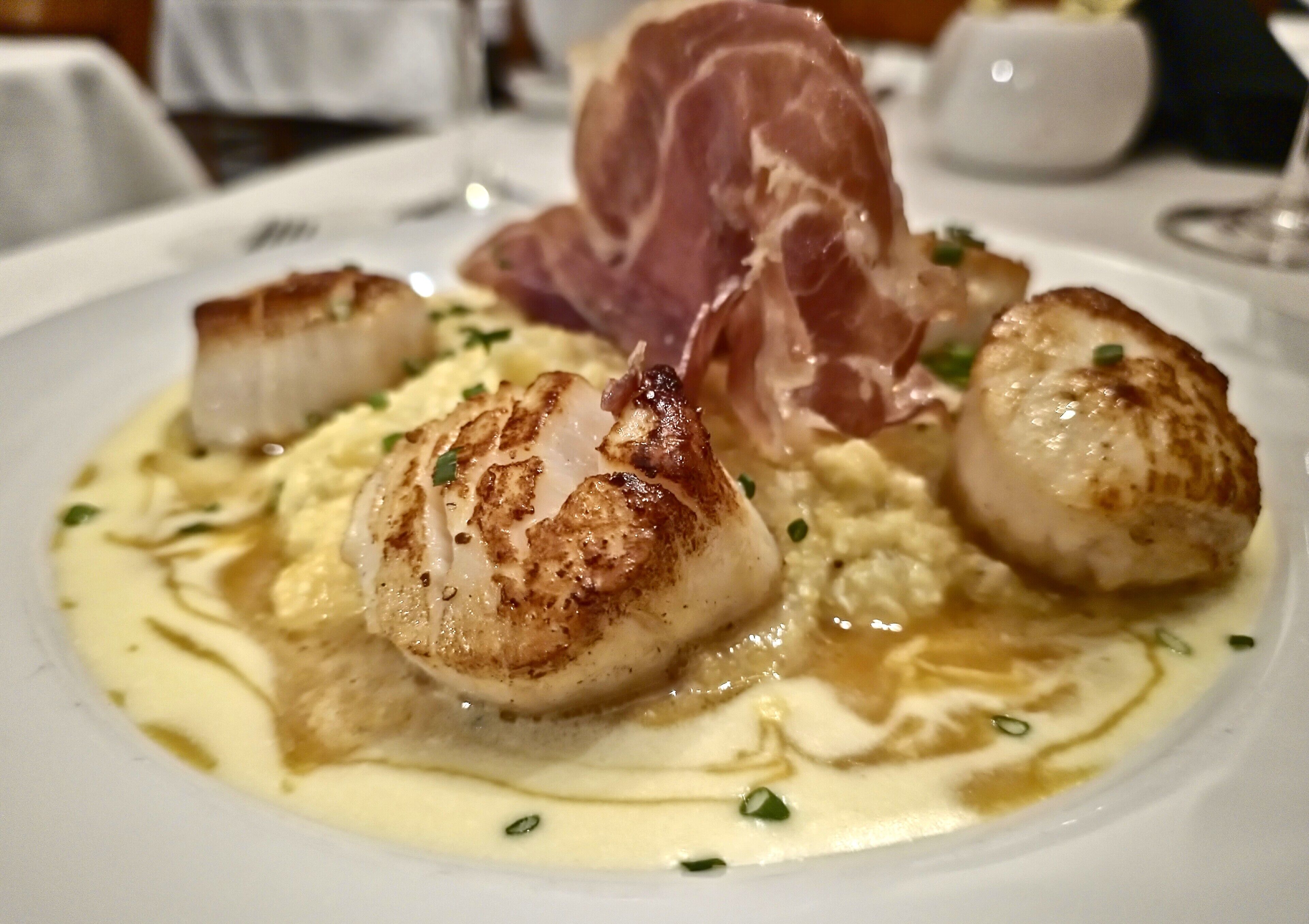 A plate of food with seared scallops, prosciutto, and a creamy sauce.