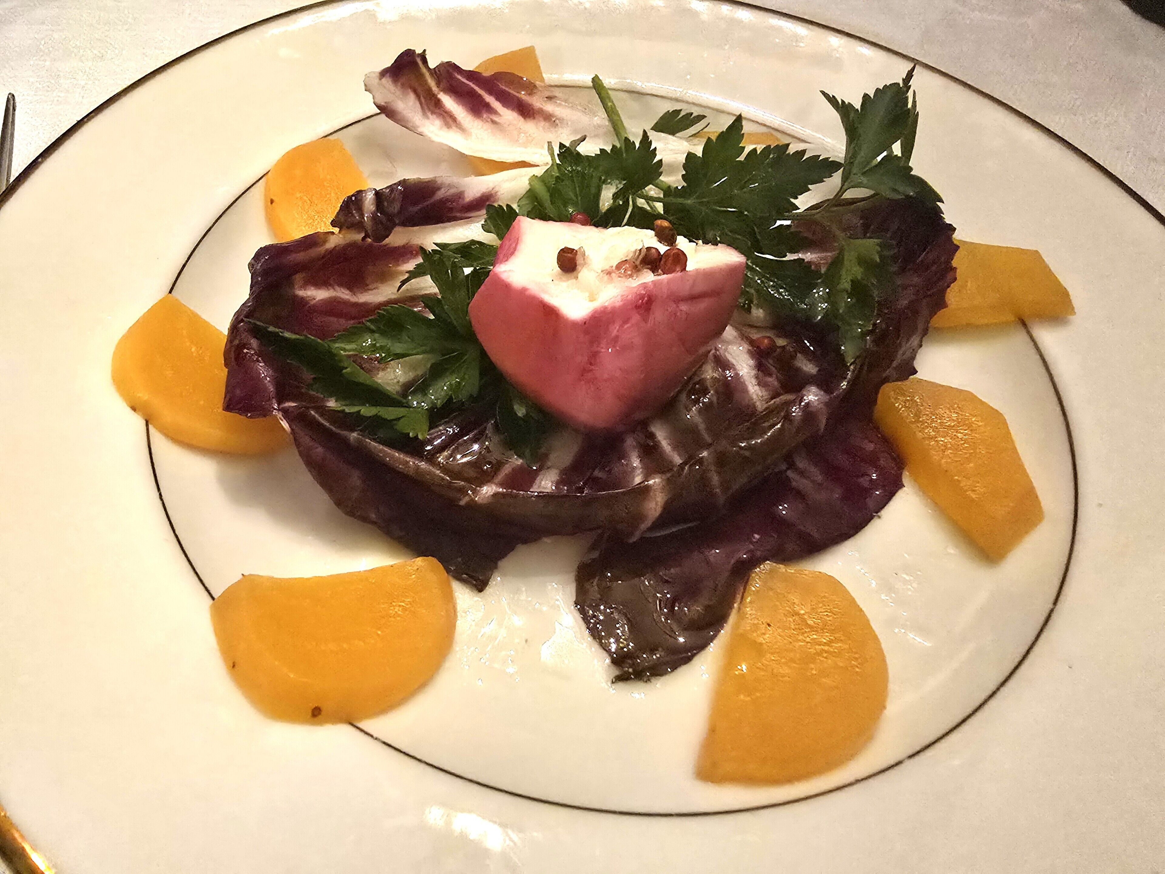 Un plato con ensalada, incluyendo hojas verdes, algo rosado y gajos de naranja.