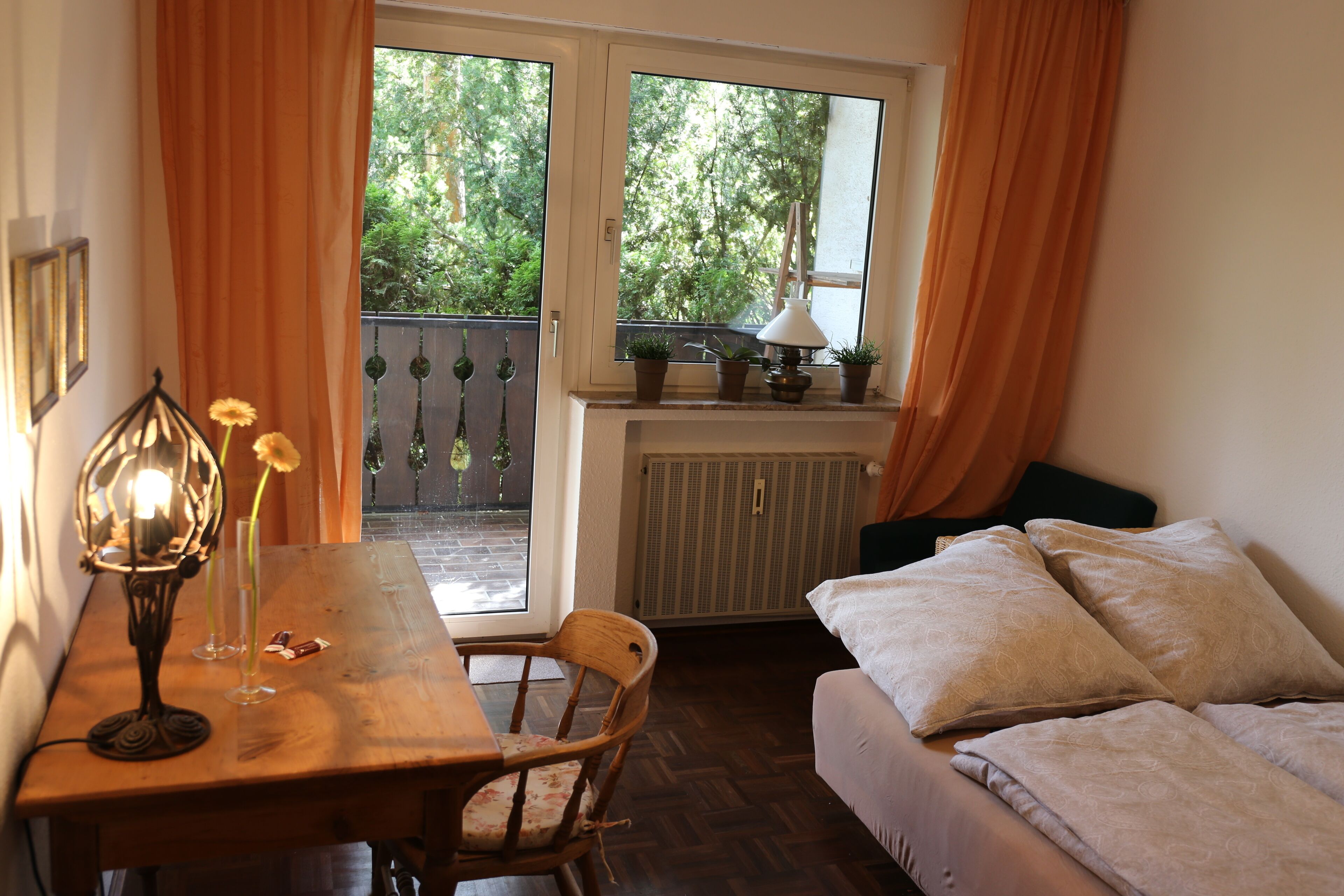 Une pièce chaleureuse avec une table en bois, une chaise, un lit avec des oreillers, une fenêtre avec des rideaux et un radiateur.