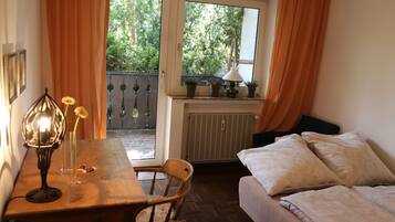 Une pièce chaleureuse avec une table en bois, une chaise, un lit avec des oreillers, une fenêtre avec des rideaux et un radiateur.