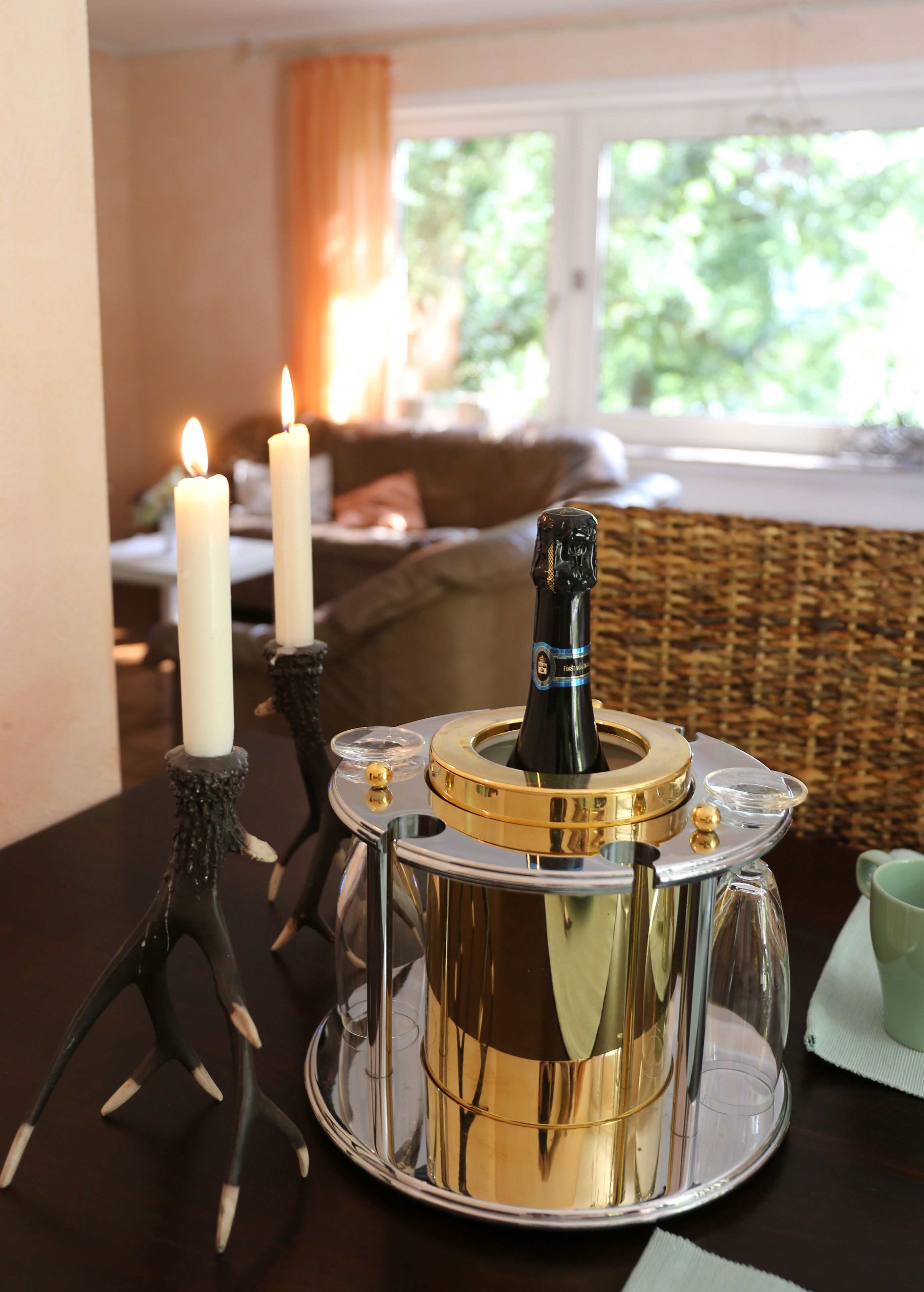 A table with a decorative champagne bottle holder, two lit candles, and a green cup.