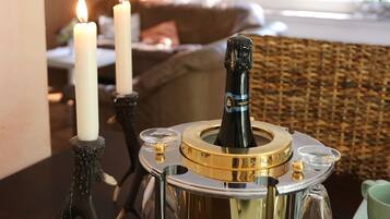 A table with a decorative champagne bottle holder, two lit candles, and a green cup.