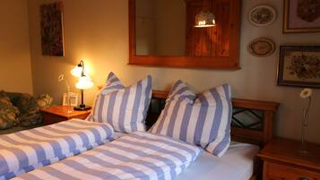 Une chambre à coucher avec un lit double, une literie à rayures, une table de chevet avec une lampe, une tête de lit en bois, un miroir et des tableaux encadrés accrochés au mur.
