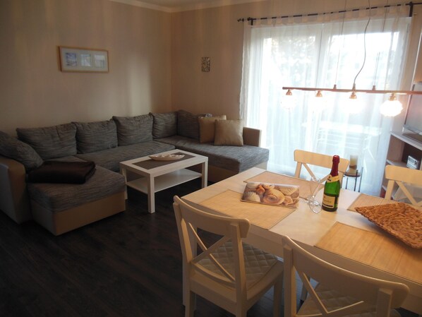 A living room with a sofa, coffee table, dining table, chairs, and a bottle of wine. - Morgenstern fantastic holiday (Göhren)