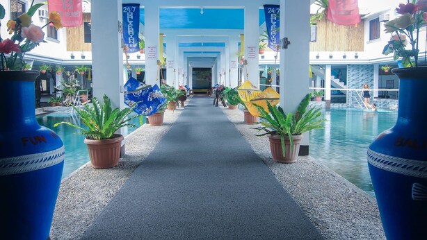 Un hall d’hôtel avec un chemin central menant à un espace piscine, entouré de plantes en pot et d’éléments décoratifs.