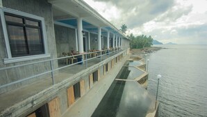 Un hôtel situé au bord de l’eau, doté d’un balcon couvert, d’un espace extérieur aménagé et offrant une vue sur la mer.