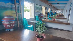 Un long couloir avec un banc en bois, des chaises de couleur turquoise et une plante en pot.