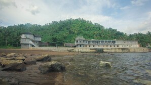 Un hôtel au design moderne, situé au bord d’une rivière, avec en toile de fond une végétation luxuriante et une colline.