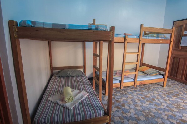 A room with three bunk beds, each with a wooden frame and striped bedding.