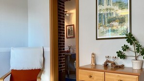 A room with a wooden chair, a wooden dresser, a framed picture on the wall, and a doorway leading to another room.