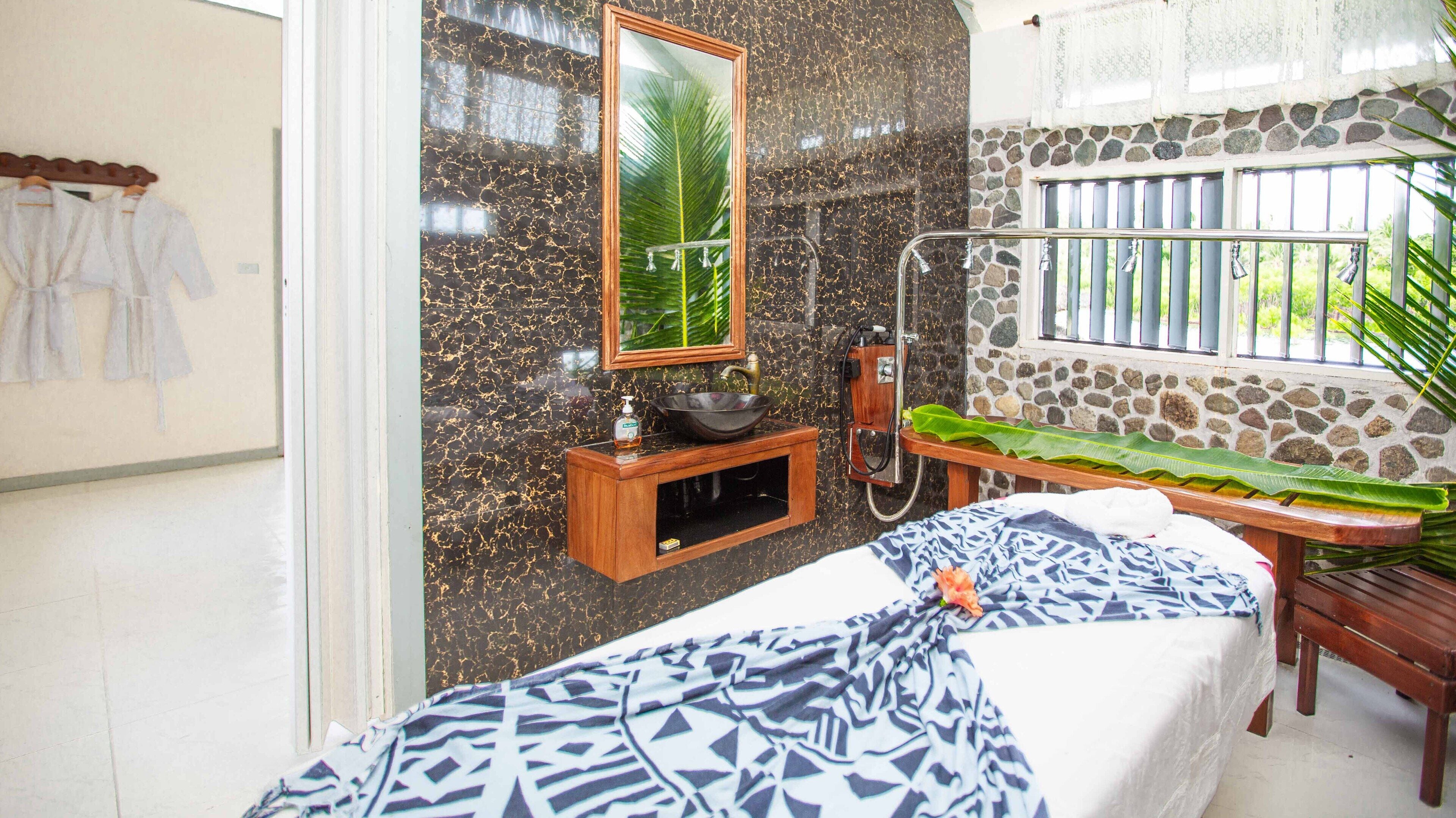 A bathroom with a large mirror, a stone wall, a wooden bench, and a window with bars.