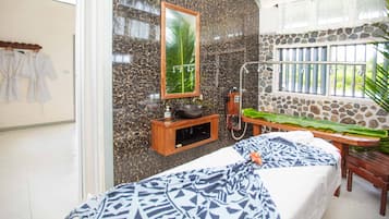 A bathroom with a large mirror, a stone wall, a wooden bench, and a window with bars.