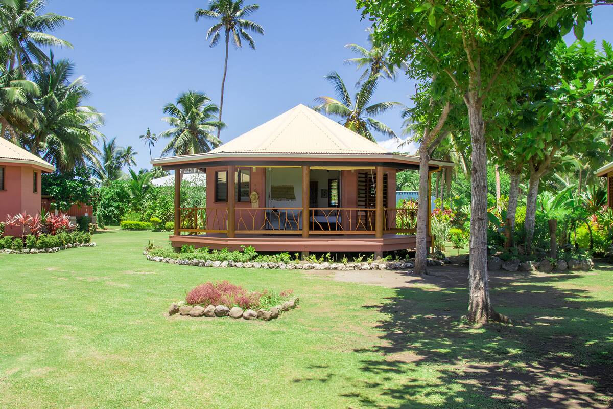 A gazebo-style structure with a covered porch, surrounded by a well-maintained lawn and tropical vegetation.
