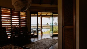 A room with a bed, a chair, a table, and a view of the ocean through large windows. - La Dolce Vita Holiday Villas (Savusavu)