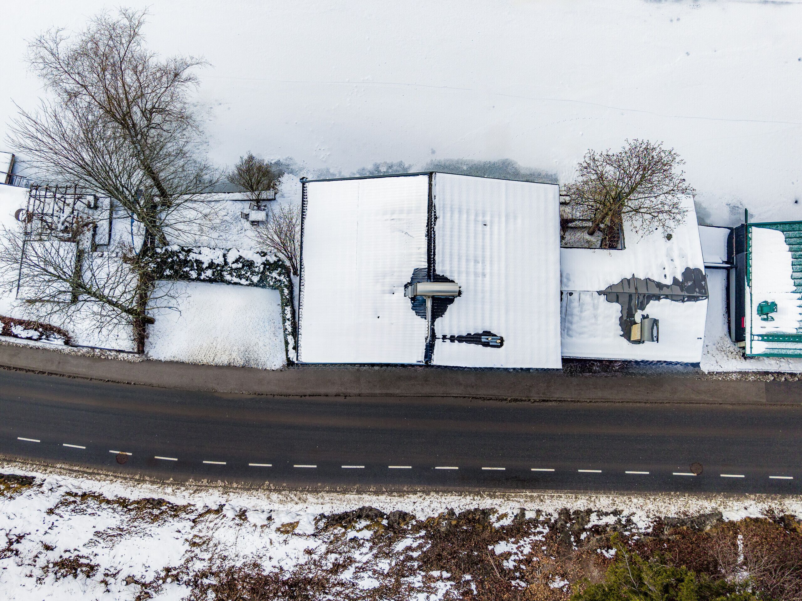 A snow-covered building adjacent to a road, with a visible security camera and a green gate.
