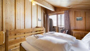 A wooden cabin room with a bed, a chair, and a window with curtains.
