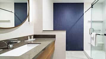 A modern bathroom with a large mirror, two sinks, a shower, and a towel rack.