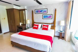 A neatly made bed with a red and white bedspread, two pillows with the word "OYO" on them, a wooden headboard, and a nightstand with a lamp. - OYO 394 Nana Beach Cha Am (Cha-am)