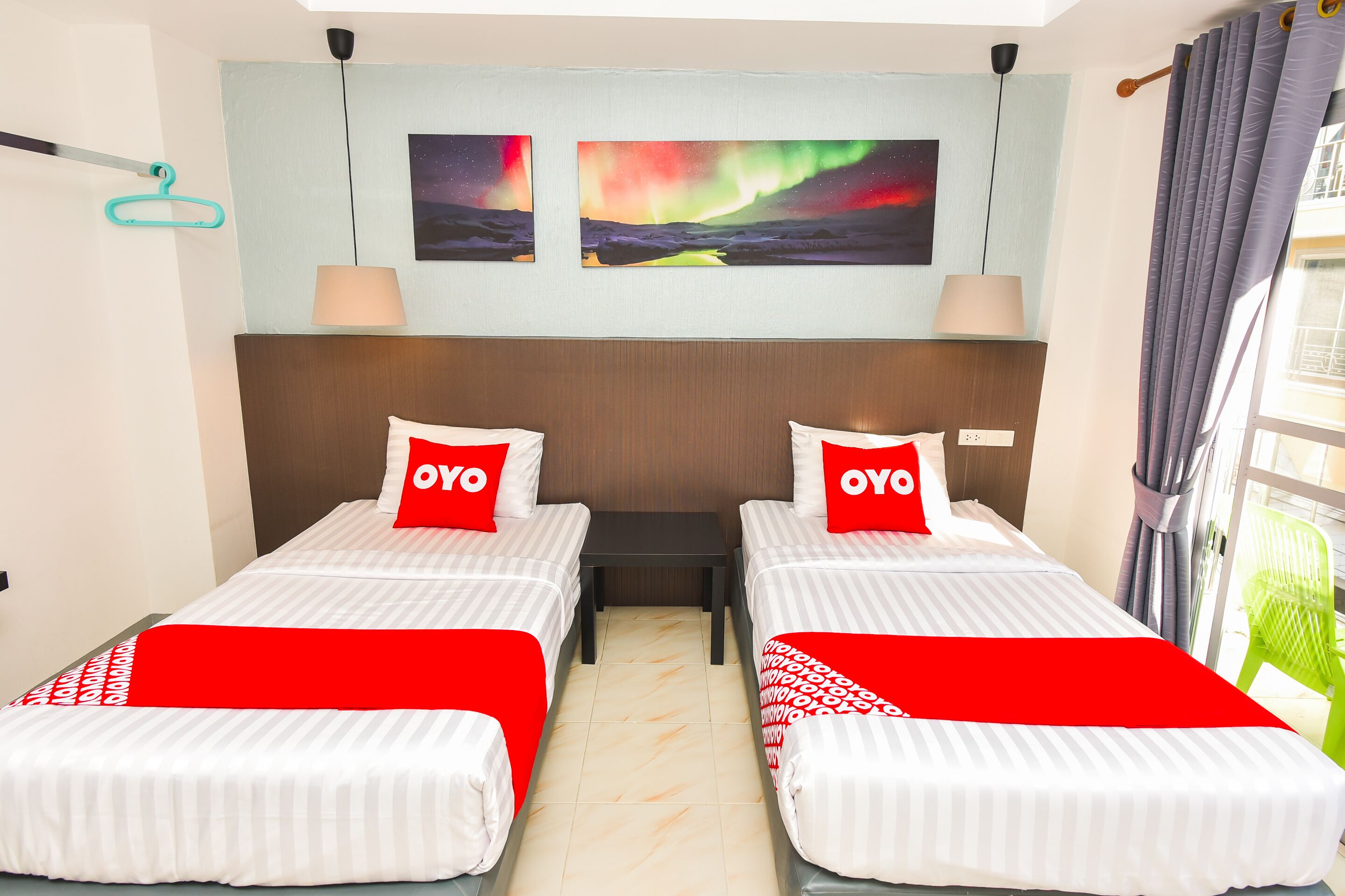 A hotel room with two beds, each with a red and white bedspread and pillows with the word "OYO". There are two wall-mounted paintings depicting the Northern Lights.