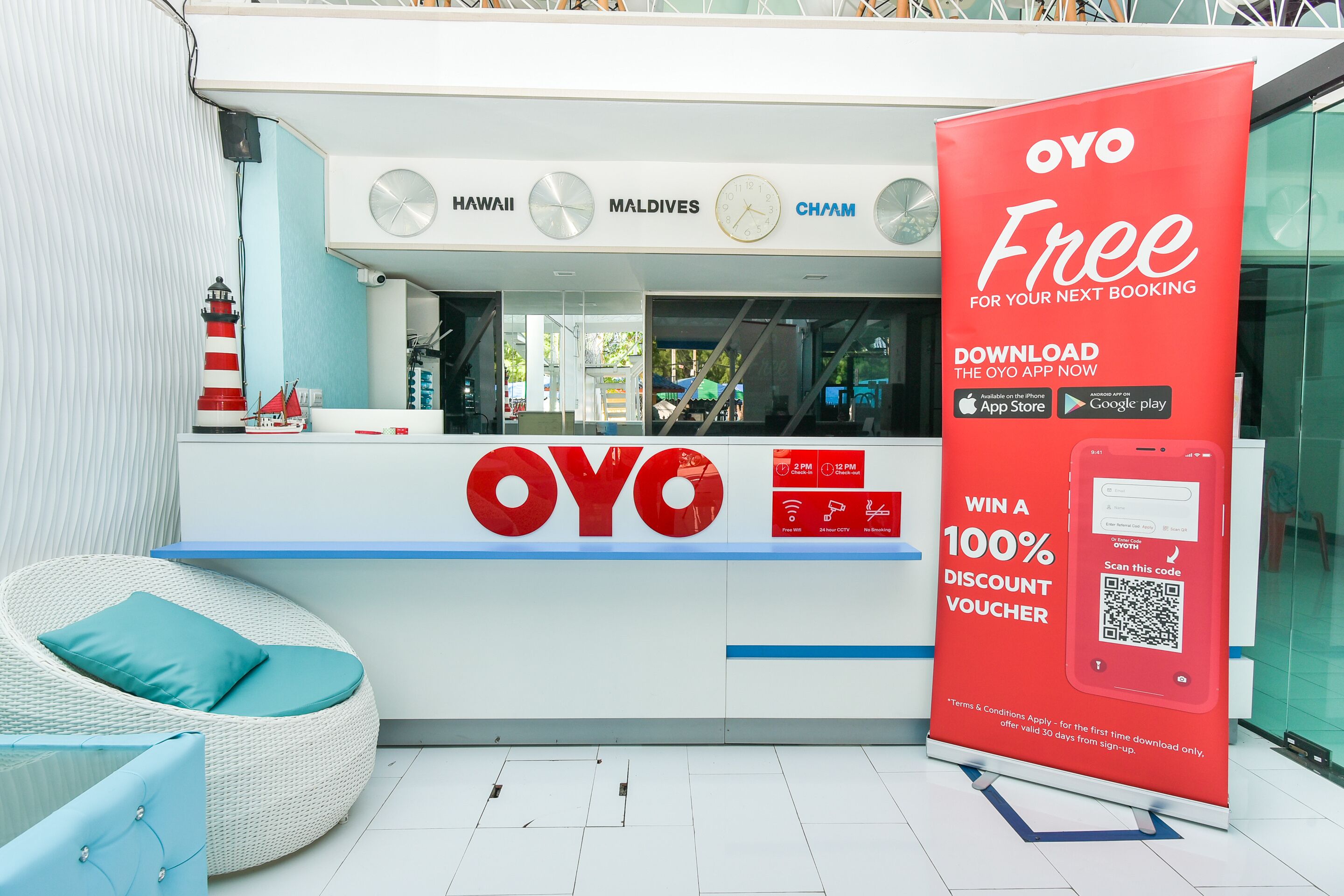 Een hotel receptie met een groot OYO bord, een fauteuil en een QR-code voor een kortingsbon.