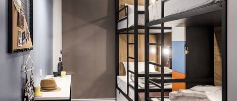 A bunk bed room with a desk, a hanging light, and a corkboard on the wall.