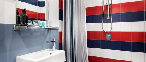 A bathroom with a white sink, a mirror, and a shower with a striped tile wall.