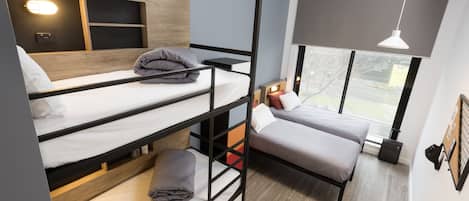 Una habitación moderna con varias camas, literas, un escritorio y un amplio ventanal con vistas al exterior.