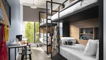 A modern, compact room with a bunk bed, a desk with a laptop, and a small seating area.