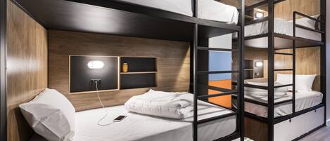 Habitación con literas, cabecera de madera, mesita de noche con lámpara y una ventana pequeña.