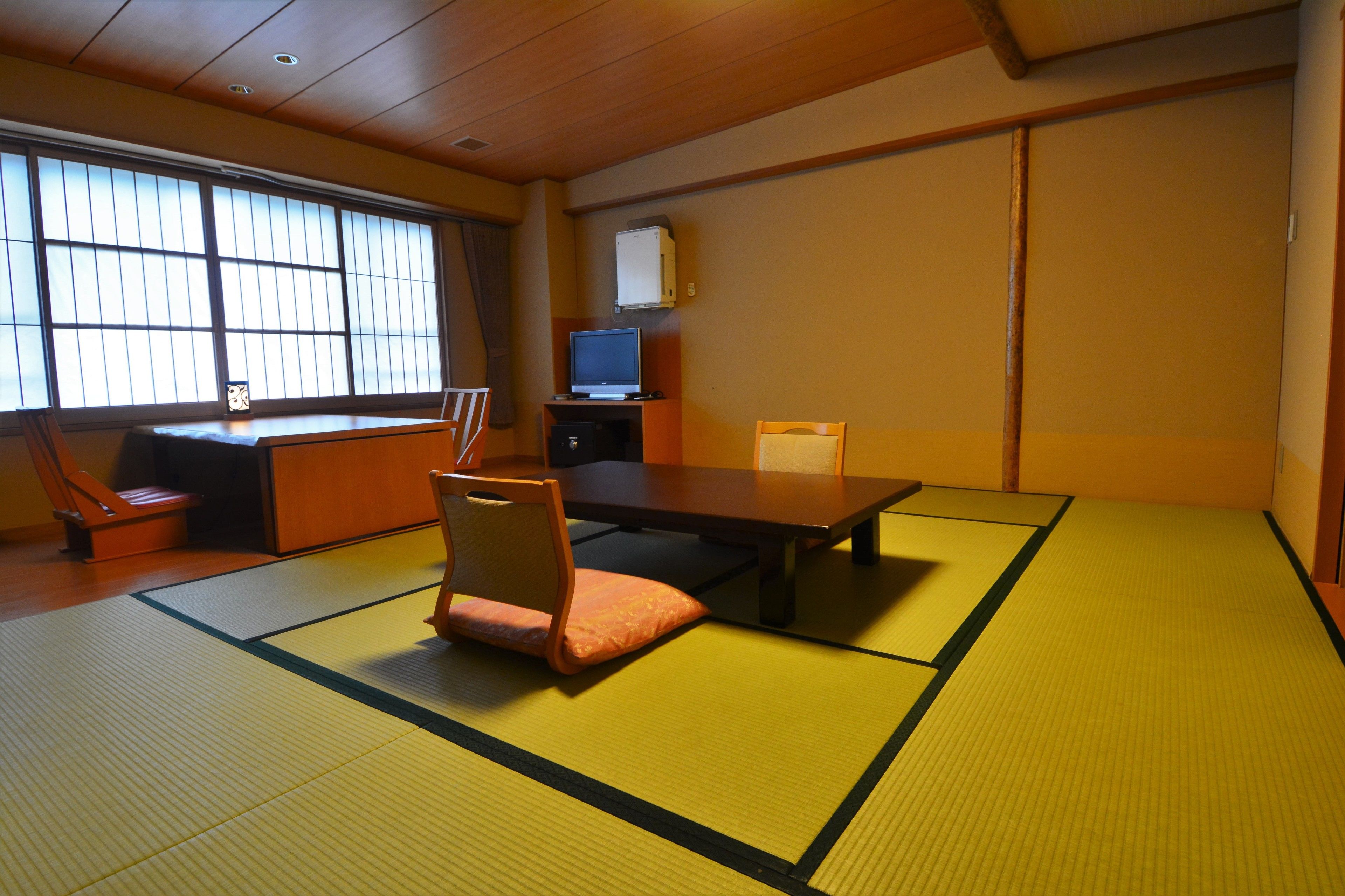 A tatami mat room with a low table, chairs, a television, and a cabinet.