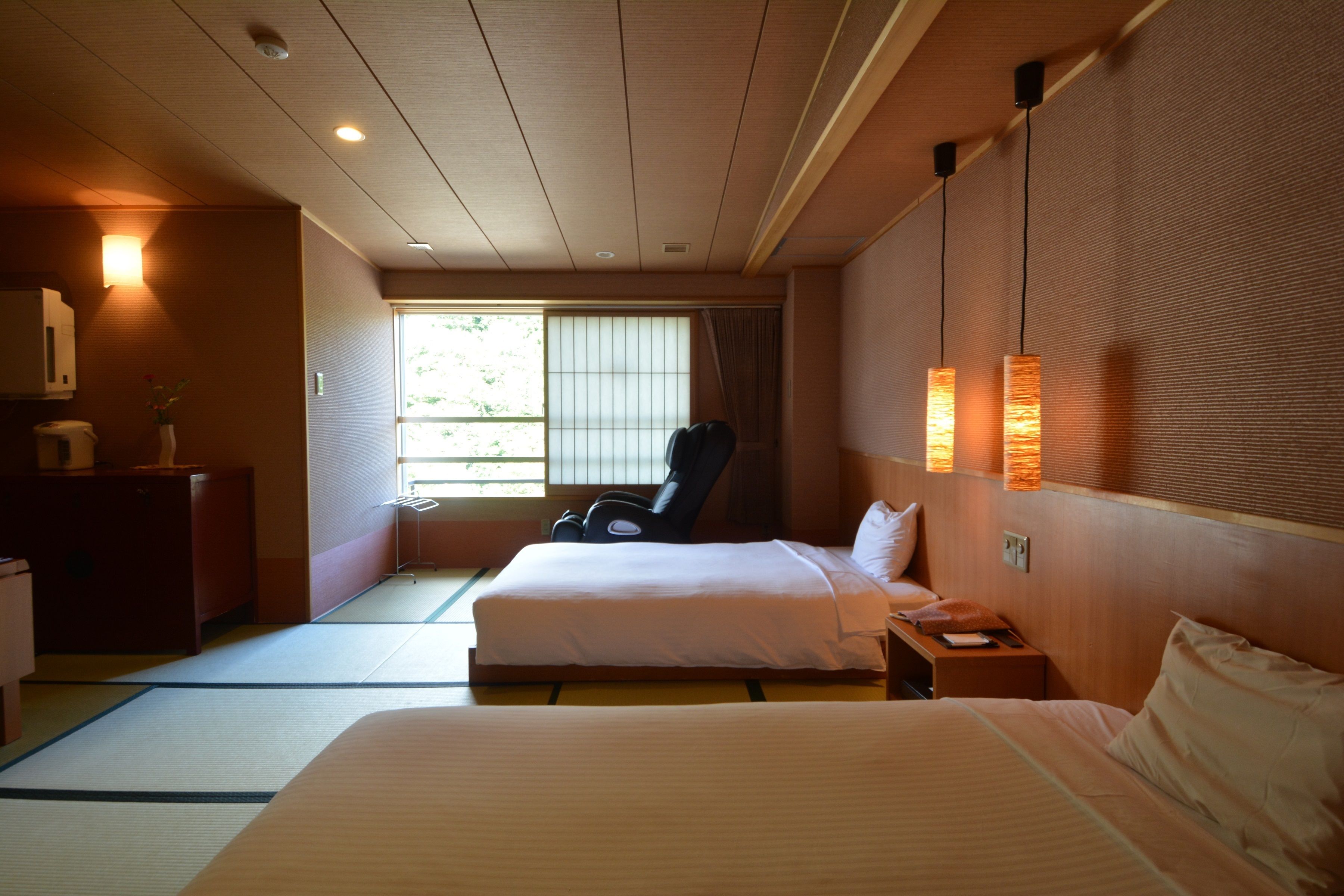 A hotel room with a bed, a chair, a bedside table, and a window with blinds.
