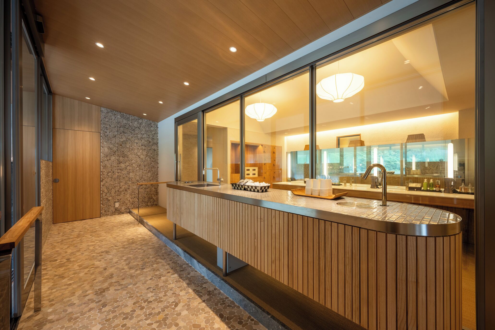 A modern kitchen with a large island, a stone wall, and a view of the adjacent living area.