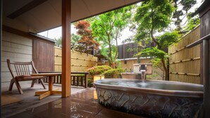 Ein traditioneller japanischer Raum mit Tatami-Böden, einem Holzsessel, einer Steinecke für ein Heißwasserbad und Bambus-Zäunen.
