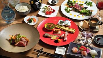 A variety of dishes on a wooden table, including sushi, sashimi, and a red plate with vegetables and meat.