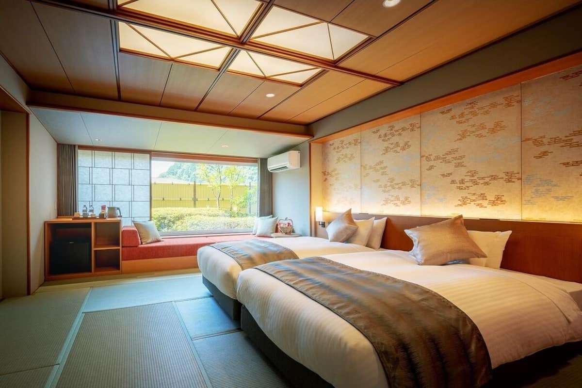 Una habitació d'hotel amb estètica tradicional japonesa, que destaca per un paviment de tatami, un sostre de fusta baix i una porta corredissa que dona a un balcó.