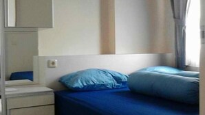 A bedroom with a bed, a nightstand, a mirror, and a window with curtains. - Kemang View Apartment (Bekasi)