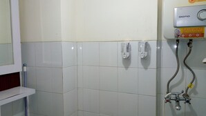 A bathroom with white tiles, a shower with a hose, and a wall-mounted water heater. - Kemang View Apartment (Bekasi)