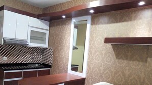 A compact kitchen with white cabinets, a microwave, and a patterned backsplash. There is a bar area with stools and a sofa. - Kemang View Apartment (Bekasi)