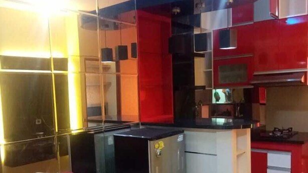 A compact kitchen with a red and white color scheme, a small refrigerator, and a sofa in the corner. - Kemang View Apartment (Bekasi)