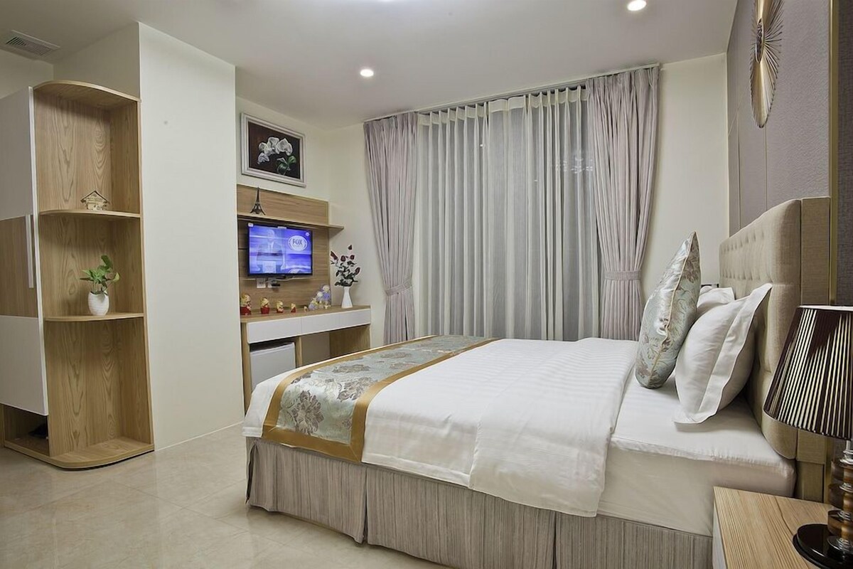 Een slaapkamer met een bed, een televisie, een bureau en een plank met decoratieve objecten.