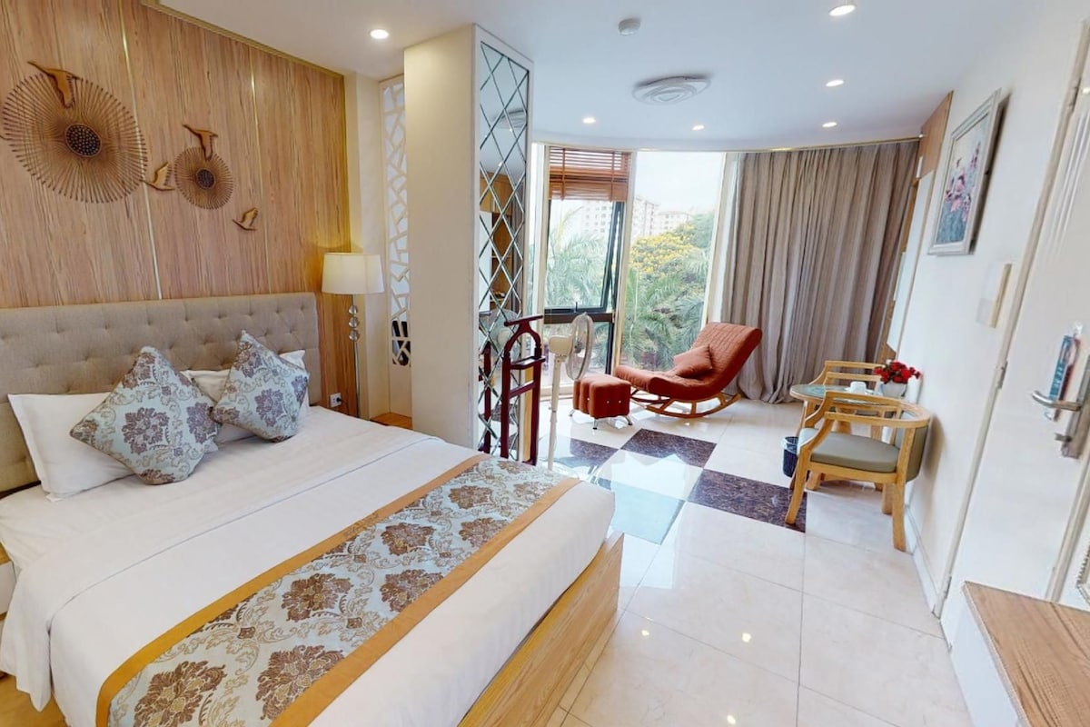 A hotel room with a large bed, a desk, a chair, and a view of the outdoors.