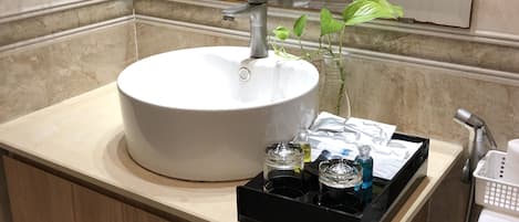A bathroom with a white sink, a mirror, a faucet, a plant, and a tray with toiletries.