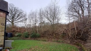 A grassy yard with a stone wall and leaf-covered ground. - Orchard Cottage (Stoke-on-Trent)