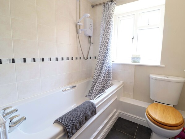 A bathroom with a bathtub, a showerhead, a toilet, and a window with a view. - Peniarth (Oswestry)