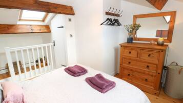 A bedroom with a skylight, a wooden dresser, a mirror, and a bed with towels.