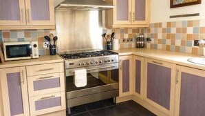 A kitchen with a gas stove, oven, microwave, and wooden cabinets. - Grace Cottage (Buckie)