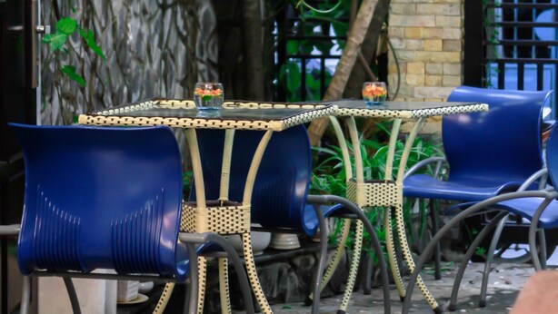 An outdoor seating area with blue chairs and a table, surrounded by greenery and a brick wall. - Hana Homestay Danang (Da Nang)