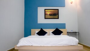 A bed with white linens and two black pillows, a framed picture of a sunset on the wall, and a small shelf with toiletries. - Hana Homestay Danang (Da Nang)